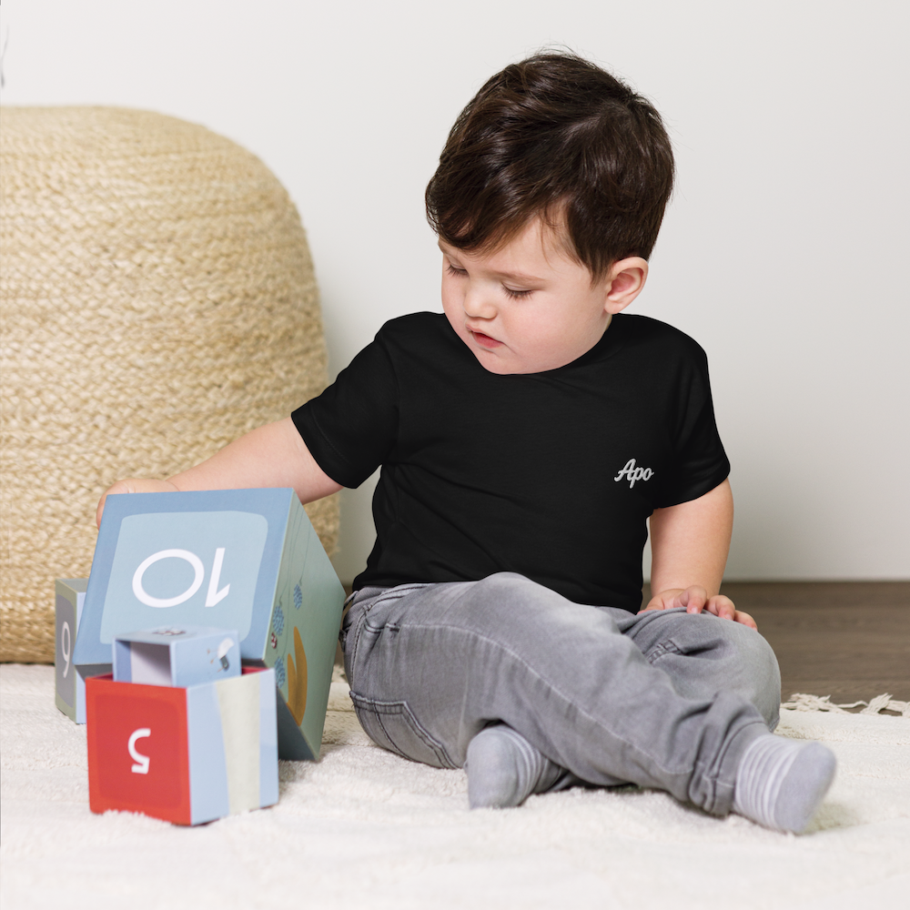 Toddler playing with blocks while wearing a black Apo (Grandchild) toddler t-shirt with white embroidered name on the left chest