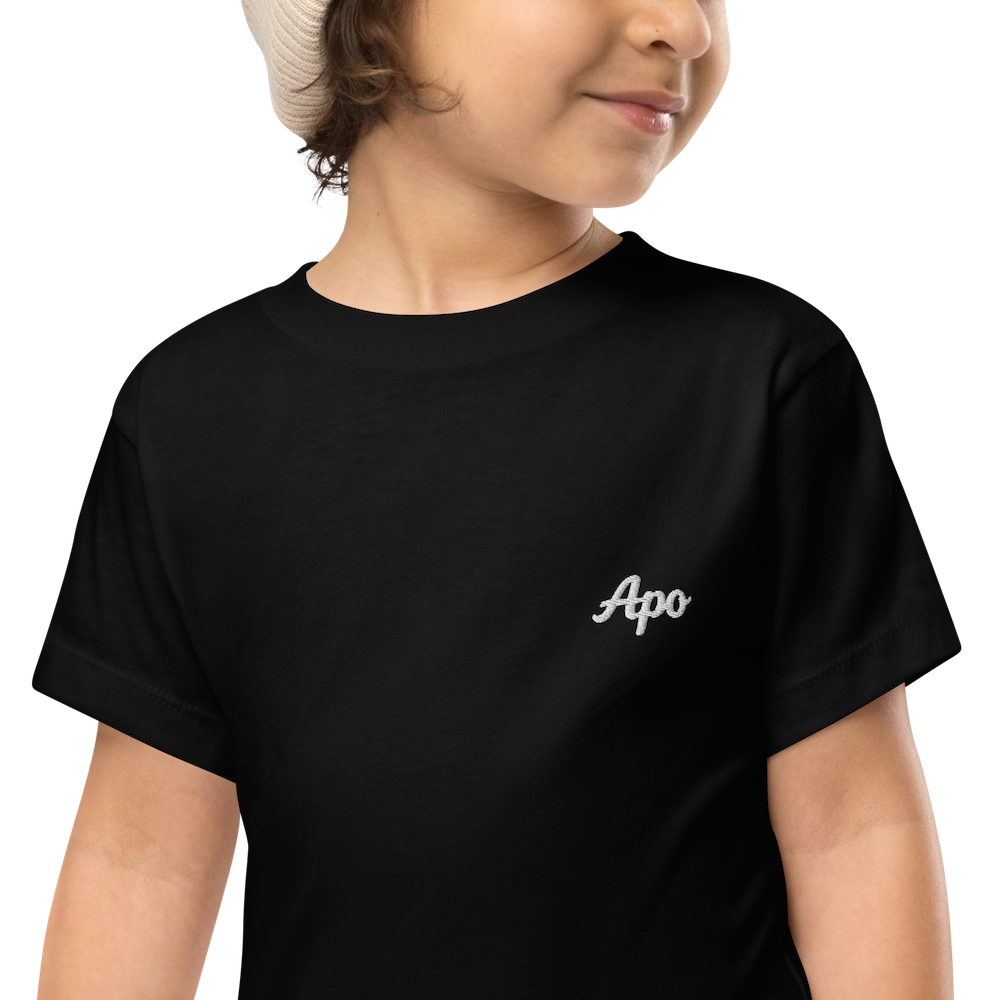 Toddler wearing a black Apo (Grandchild) toddler t-shirt with white embroidered name on the left chest, close-up